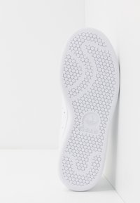 Vit sneakersula med ett strukturerat hexagonmönster, släta kanter och präglad logotyp. Minimalistisk design som fokuserar på funktionalitet.