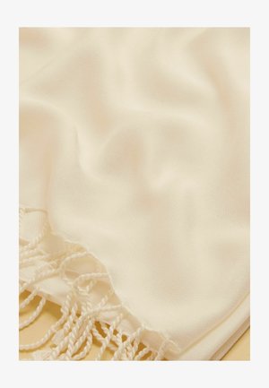 Kreemikas kangas, pehme tekstuuriga ja ühe serva ääres keerutatud sõlmedega, suures plaanis õrnade voltidega.