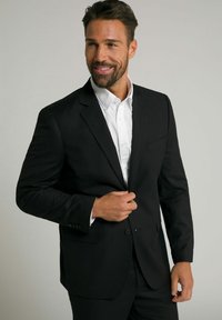 Chaqueta de traje negra hecha de tela suave, con cierre de un solo botón, solapas de muesca y un bolsillo en el pecho, llevada sobre una camisa blanca.