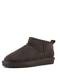 Bottine en cuir suédé marron avec un bout arrondi, un col court et une semelle plate en caoutchouc dotée d'un motif de griffes en zigzag. Détail de couture sur les coutures latérales.