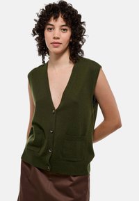Gilet sans manches vert, design en V, deux poches avant, cinq boutons foncés, taille côtelée, texture en tricot douce.