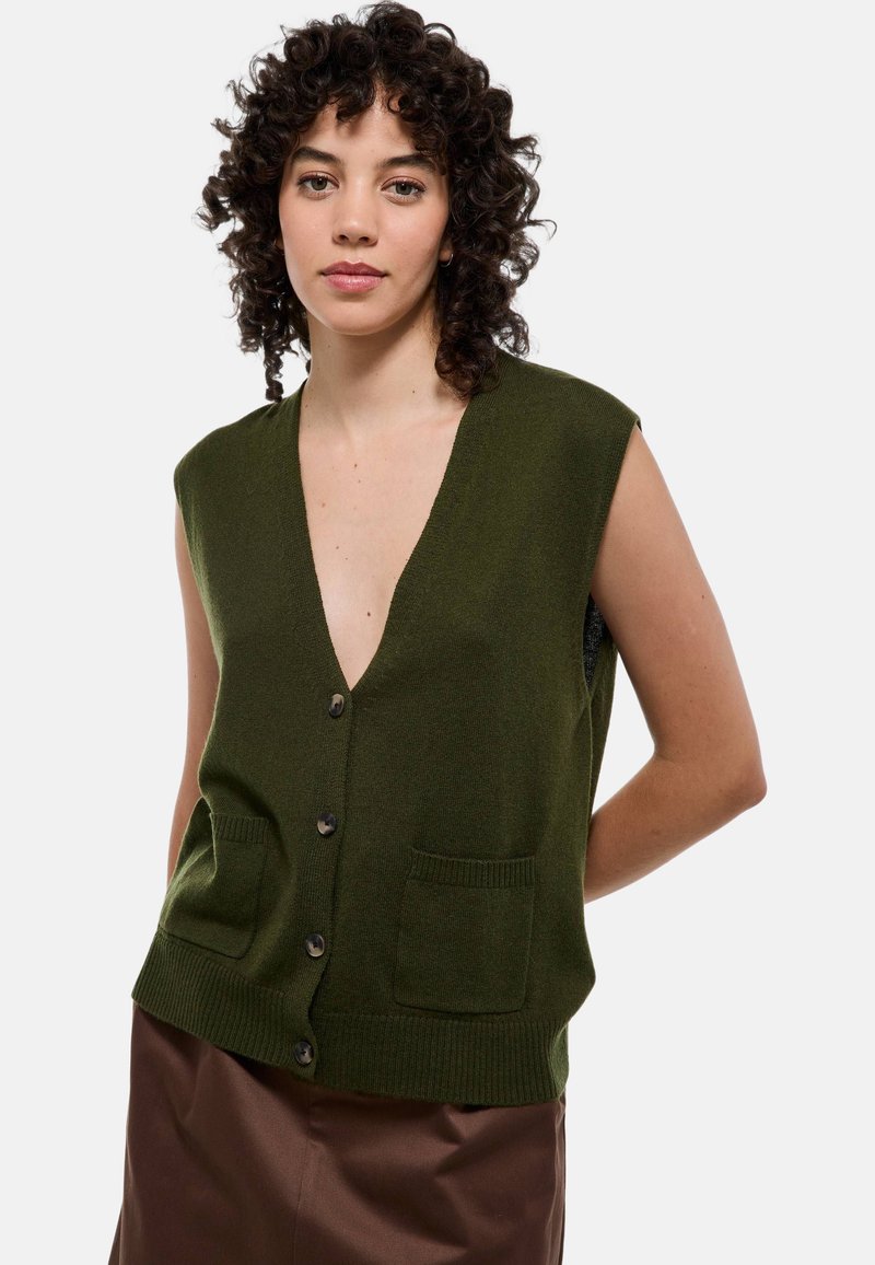 Gilet sans manches vert, design en V, deux poches avant, cinq boutons foncés, taille côtelée, texture en tricot douce.