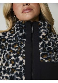 Giacca in pile con stampa leopardata nei toni del blu scuro, beige e marrone. Presenta una chiusura con zip nera e un design con colletto alto.