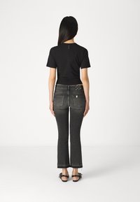 Svart kortermet topp kombinert med høyt talje, utsvingte mørkegrå jeans med et dekorativt design på baklommen og rå kant.