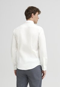 White long-sleeve shirt with a spread collar, smooth texture, and buttoned cuffs, paired with gray pinstriped trousers.