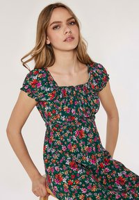 Vestido floral con mangas cortas abullonadas, de tejido verde, adornado con flores multicolores. Presenta un cuerpo fruncido y un corte relajado.