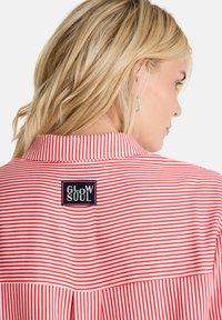 Red and white striped shirt with a collared neck, featuring a black "GLOW SOUL" logo patch on the back. Smooth fabric texture, casual design.