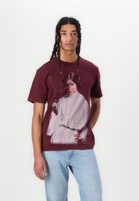 Maroon cotton t-shirt featuring a graphic design of a female character holding a blaster, short sleeves, and a relaxed fit.