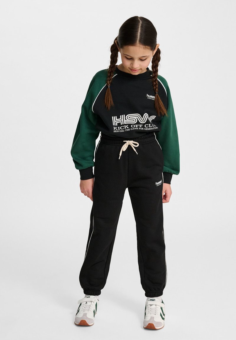 Schwarze Jogginghose mit weißen seitlichen Streifen und verstellbarem Kordelzug. Grünes Langarmoberteil mit schwarzen Akzenten und bedrucktem Text.