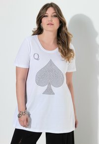 Camiseta blanca de manga corta con un gran diseño de trébol negro hecho de rhinestones, con una pequeña "Q" encima del trébol. Textura de tela suave.