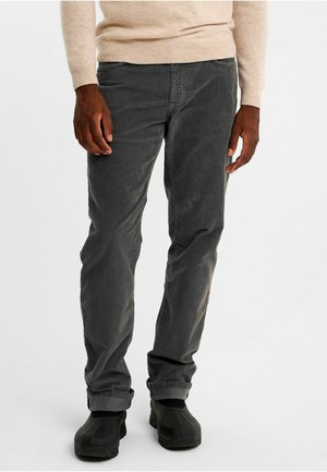 Mörkgrå kordtäckbyxor med vertikala ribbor, slim fit, vikta fållar, bärs med svarta gummisulade skor. Texturerad tyg synlig.