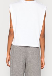 Top bianco senza maniche con una vestibilità comoda, scollatura rotonda e orlo corto, abbinato a pantaloni in tessuto grigio chiaro caratterizzati da una sottile texture.