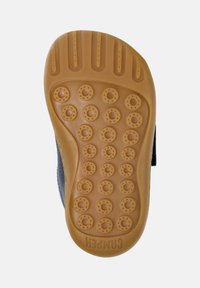 Vue inférieure d'une semelle de chaussure d'enfant avec des motifs de grip circulaires et le nom de la marque "Camper" embossé au talon.