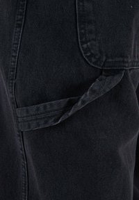 Pantaloni in denim neri con una finitura texturizzata, dotati di una tasca laterale e dettagli di cucitura visibili, che enfatizzano un design a vestibilità rilassata.