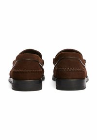 Mocassini in suede marrone con una suola nera liscia, caratterizzati da dettagli cuciti e un design classico slip-on. La vista posteriore mette in mostra bordi curvi.