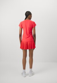 Pleated red tennis dress with short sleeves, fitted bodice, and a flared skirt. Made of lightweight fabric, features a smooth texture.