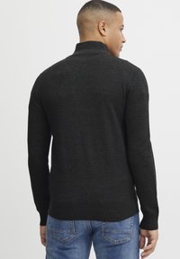 Mörk texturerad stickad tröja med hög krage och ribbade ärmslut, med en figursydd passform och diskreta sidoflikar.