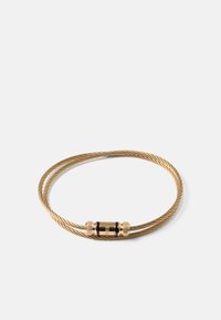 Bracelet en fil torsadé doré avec un fermoir cylindrique gravé du nom de la marque, exposé sur un fond blanc uni.