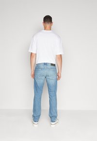 Vit kortärmad t-shirt kombinerad med ljusblå denimjeans, med rak benpassform och detaljerade bakfickor, bärs med vita skor.