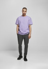 Tricou din bumbac lavandă cu mâneci scurte, asociat cu pantaloni tapered de culoare gri închis. Outfitul este completat cu adidași negri. Design simplu, fără modele.