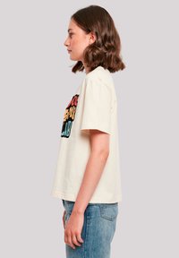 Cream cotton T-shirt featuring colorful graphical text "SCHOOL PROBLEMS CLUB" on the front, short sleeves, and a loose fit.