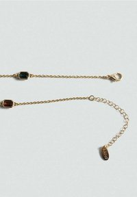 Collier délicat en chaîne d'or avec deux pierres précieuses rectangulaires vert foncé et rouge, et un fermoir ajustable avec une petite étiquette ovale.