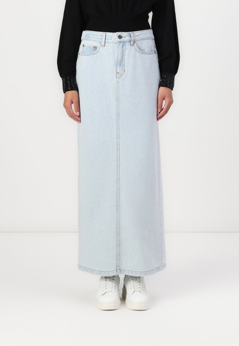 Svetlo modra denim maxi krilo s ravnim krojem, sprednjimi žepi in diskretnimi šivi, v kombinaciji z belimi supergami.