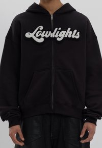 Hoodie noir à fermeture éclair avec un logo "Lowlights" blanc et duveteux. Comprend une poche avant et des poignets côtelés. Tissu doux avec une coupe décontractée.