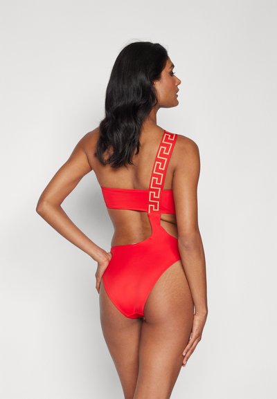 Maillot de bain une pièce rouge avec un dos découpé, doté d'une large sangle unique ornée d'un motif géométrique en or. Texture lisse.