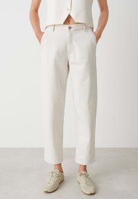 Pantalons cropped beige clair en denim, dotés d'une fermeture à bouton, de poches latérales et d'une coupe droite. Associés à des baskets grises.