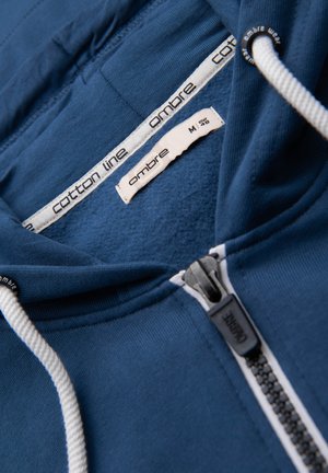 Blue cotton hoodie with white drawstrings, black zipper, and size tag marked M EUR 48 from Ombre Cotton Line.