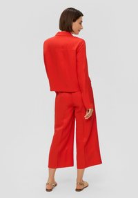 Costume en lin rouge avec une veste cropped et un pantalon à jambes larges. Texture lisse, design minimaliste, et manches courtes avec un col.