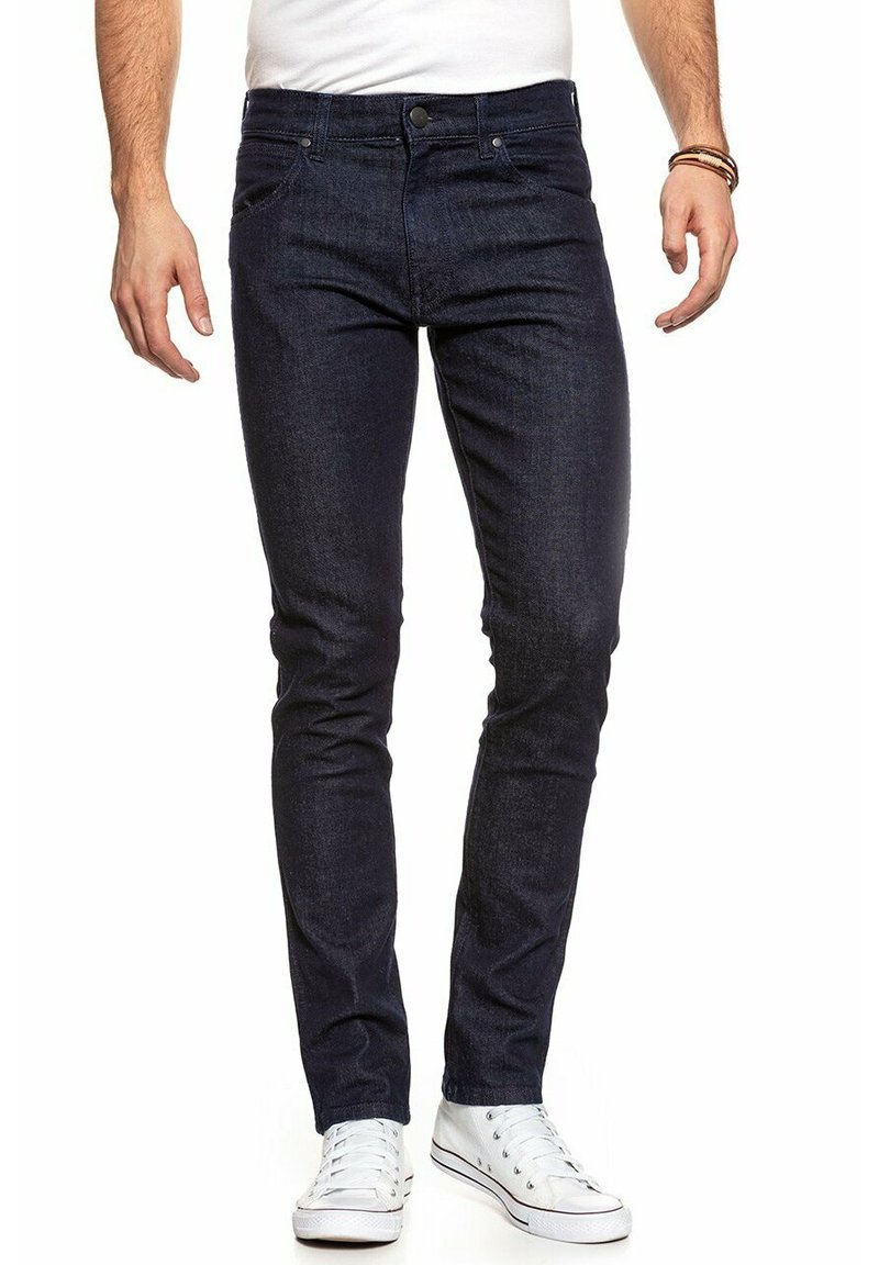 Granatowe dżinsy o dopasowanym kroju, pięć kieszeni, z przodu z zapięciem na guzik, w połączeniu z białymi trampkami. Gładka faktura.