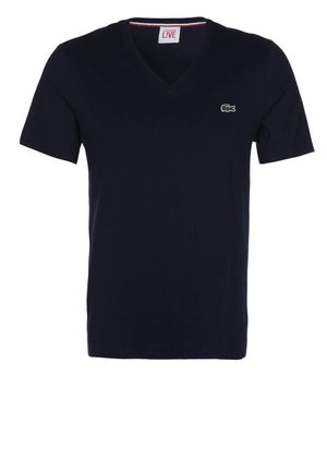 T-shirt bleu marine à manches courtes et col en V, petit logo crocodile vert sur la poitrine gauche ; design uni, sans motifs visibles.
