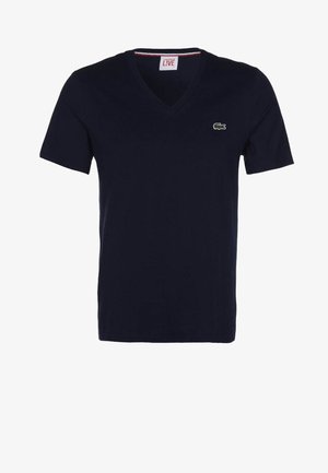 T-shirt bleu marine à manches courtes et col en V, petit logo crocodile vert sur la poitrine gauche ; design uni, sans motifs visibles.