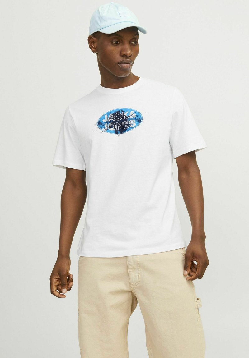 Hvid T-shirt med korte ærmer, der har et blåt og sort "JACK & JONES" logo på forsiden. Let stof med en afslappet pasform.