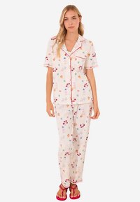 Ensemble de pyjama léger rose comprenant un haut à manches courtes et un pantalon assorti avec des motifs colorés de fruits et de fleurs ; finitions en passepoil rouge.