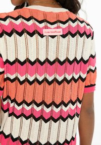Pletený top s chevron vzorem v růžové, oranžové, černé a bílé barvě, s otevřenými detaily a štítkem "CLUB TROPICANA" na zadní straně.
