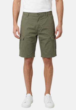 Homme portant un short cargo vert olive avec des poches à rabat sur les côtés, assorti à des baskets blanches et un t-shirt blanc, debout devant un fond blanc.