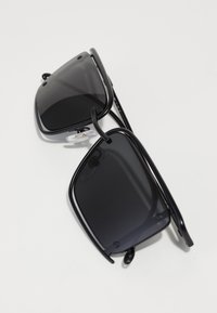 Black sunglasses with a rectangular frame, dark lenses, thin temples, and nose pads. Surface smooth with a glossy finish.