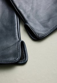 Sorte læderhandsker med glat tekstur, afrundede manchetter og kontrasterende stikninger. Materialet fremstår blødt og veludført.