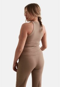 Beige ribbed tank top and matching pants, featuring a fitted design and textural detail. The top has a rounded neckline and wide straps.