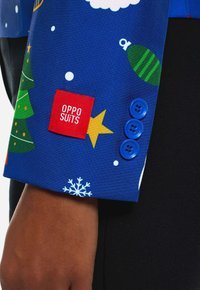 Blue festive suit jacket with Christmas patterns, red "OPPO SUITS" tag, and three blue buttons on the cuff beside a snowflake design.