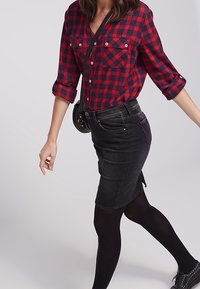 Rood en marineblauw geruit overhemd met opgerolde mouwen, gecombineerd met een zwarte denim kokerrok, gedragen met zwarte tights en een kleine schoudertas.