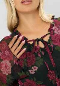 Blusa nera con fiori e scollatura arricciata. Presenta grandi fiori borgogna e foglie verdi. Si lega sul davanti, tessuto leggero e maniche svasate.