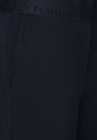 Granatowe, elastyczne dresy z gładkiego materiału, z elastycznym pasem z wytłoczonym napisem "POZYTYWNOŚĆ" i bocznymi kieszeniami.