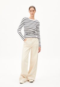 Langärmliges, schwarz-weiß gestreiftes Oberteil mit Rundhalsausschnitt, kombiniert mit weiten hellbeigen Hosen, getragen mit hellen Schuhen.