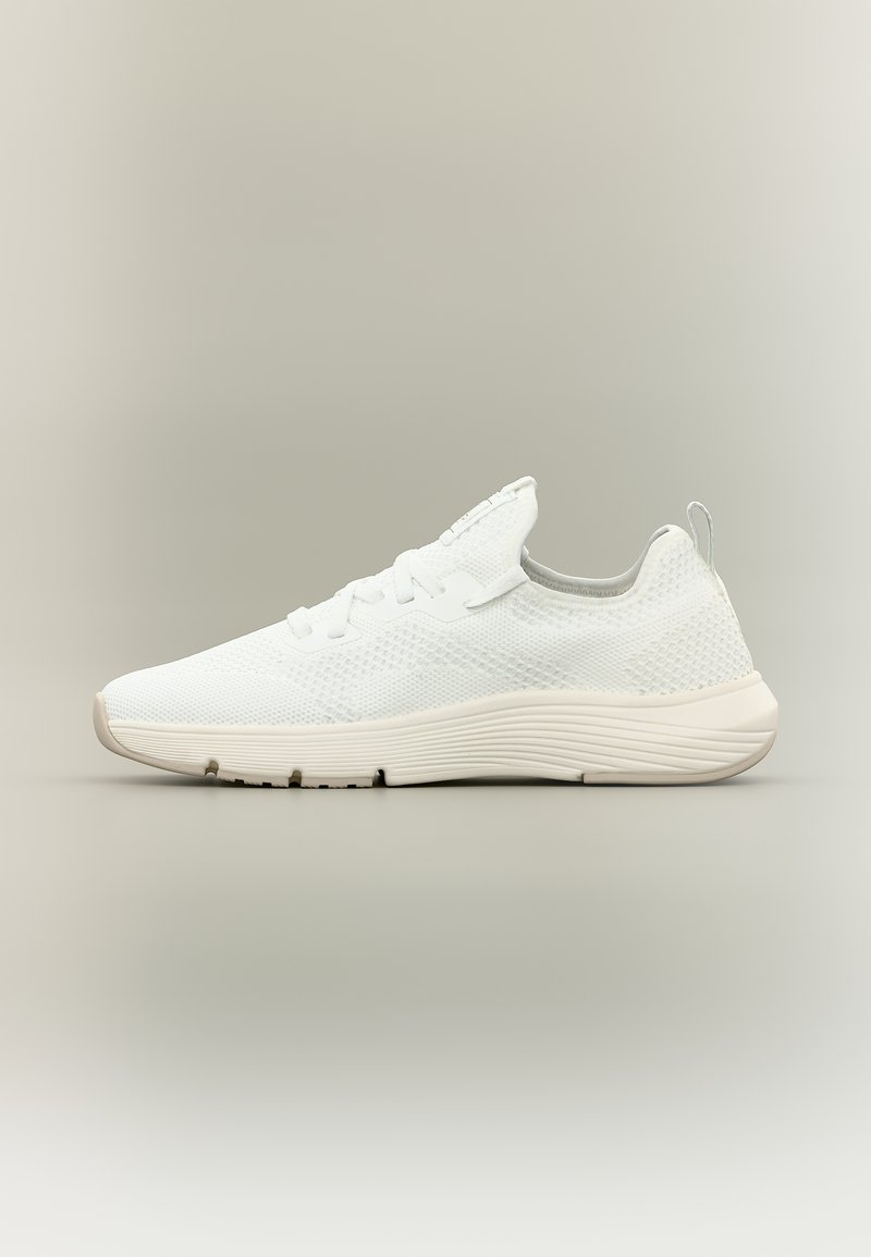 Baskets basses blanches en tricot avec semelle texturée, languette à l'arrière et fermeture à lacets sur un fond neutre.