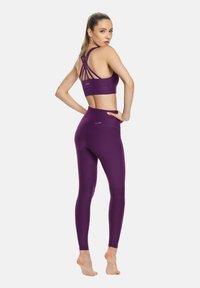 Brassière de sport violette avec un dos croisé et un legging taille haute assorti, fabriqués en matière extensible et douce.