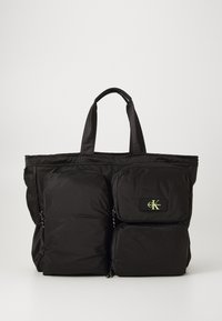 Large black nylon tote bag with dual front pockets, zip closures, and embroidered logo accent. Features sturdy handles for easy carry.
